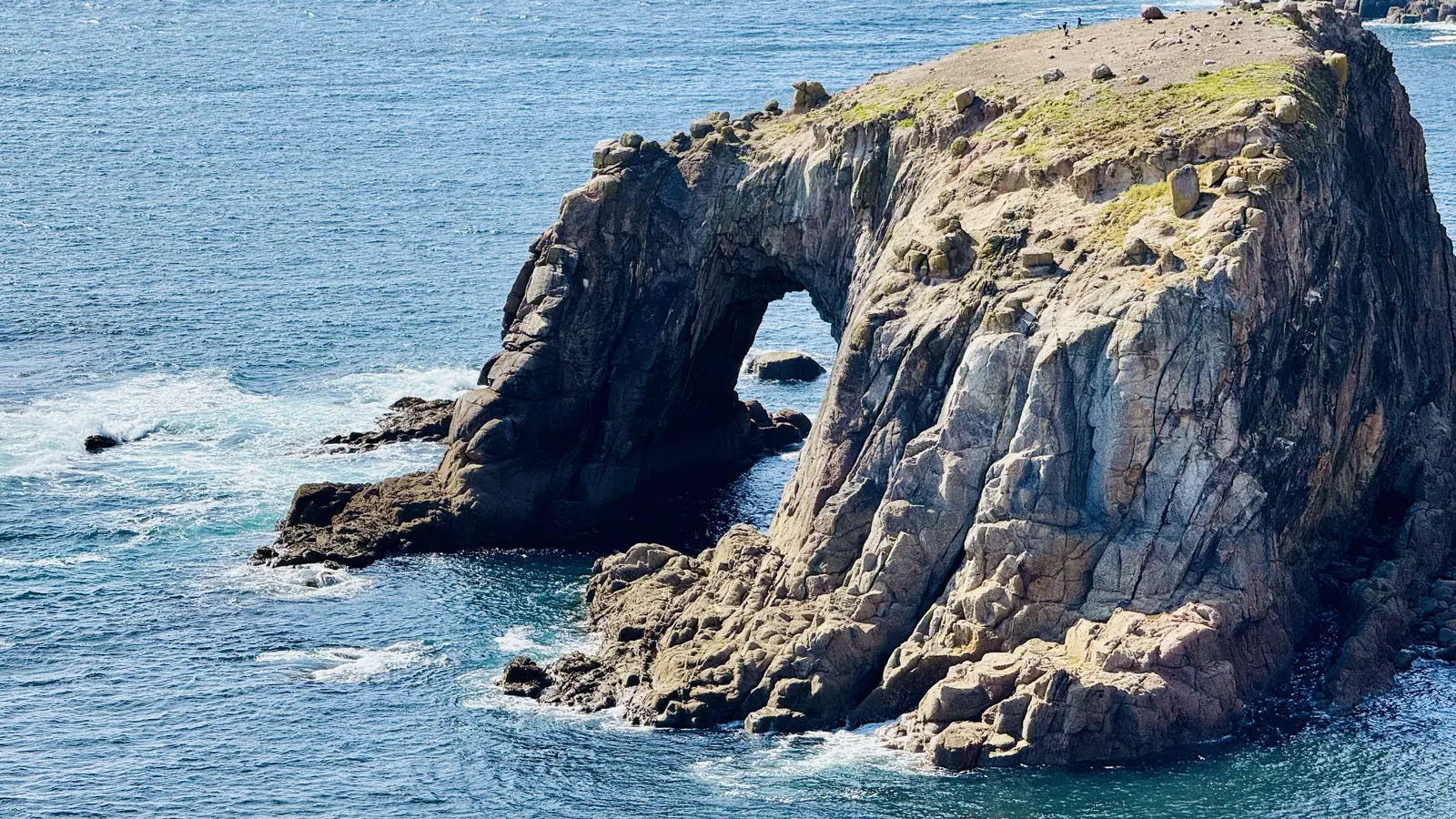 The large natural granite arch of Enys Dodnan rising from the sea south of Land's End